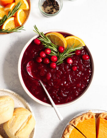 above shot of a small bowl of cranberry sauce, garnished with fresh rosemary and orange slices.