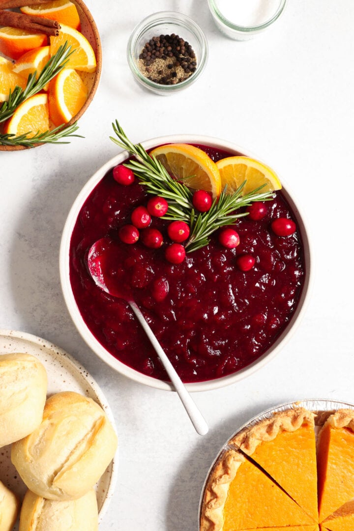 above shot of a small bowl of cranberry sauce, garnished with fresh rosemary and orange slices.