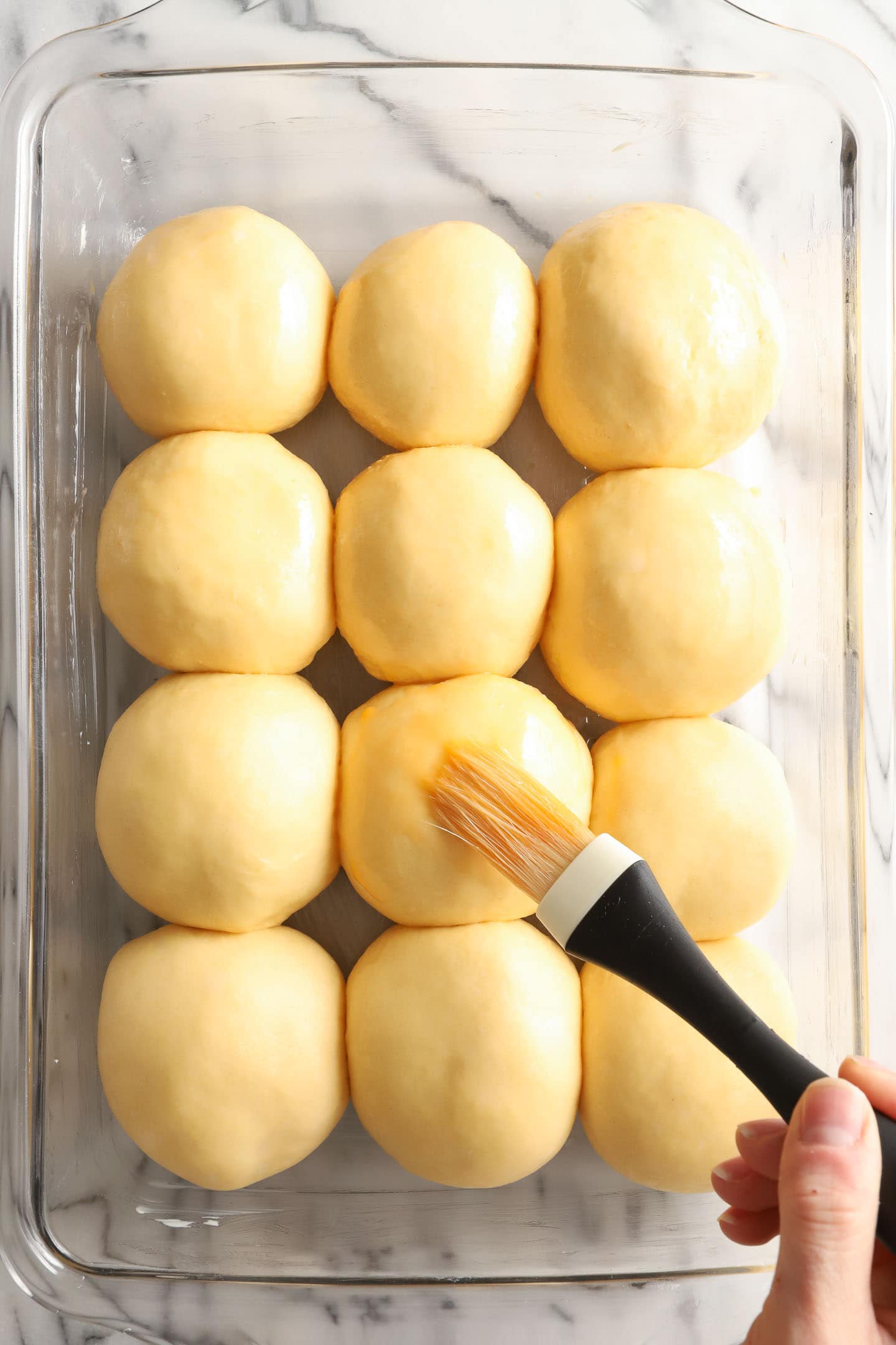 Tray of unbaked rolls being brushed with egg wash