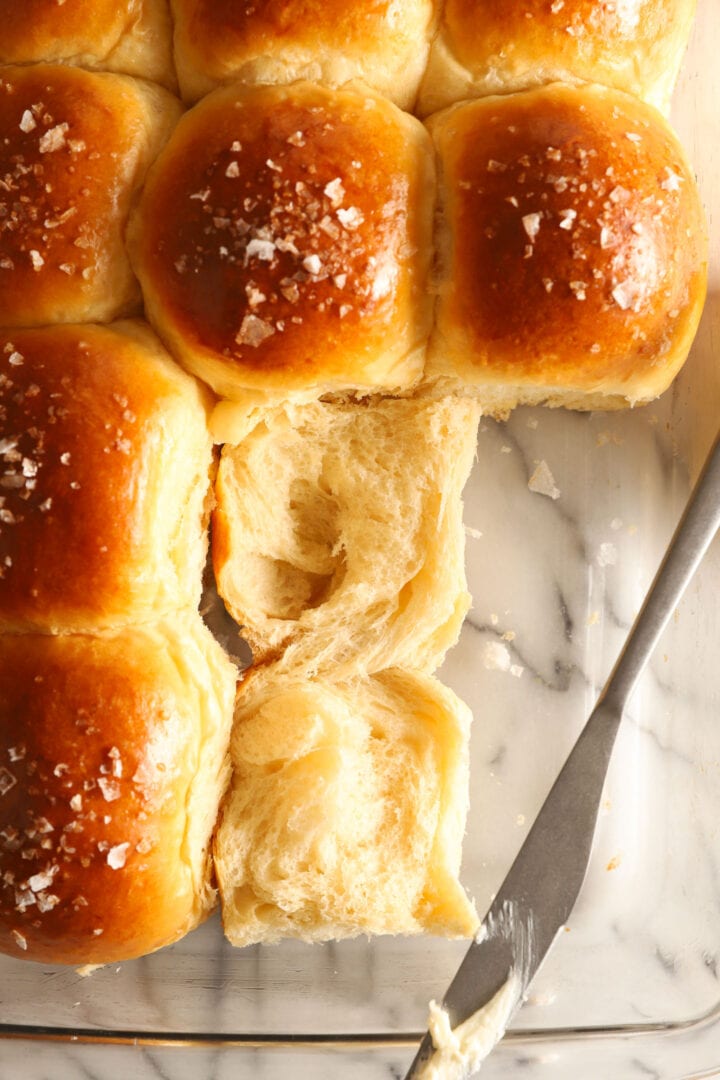 tray of dinner rolls with salt on top and a knife with butter