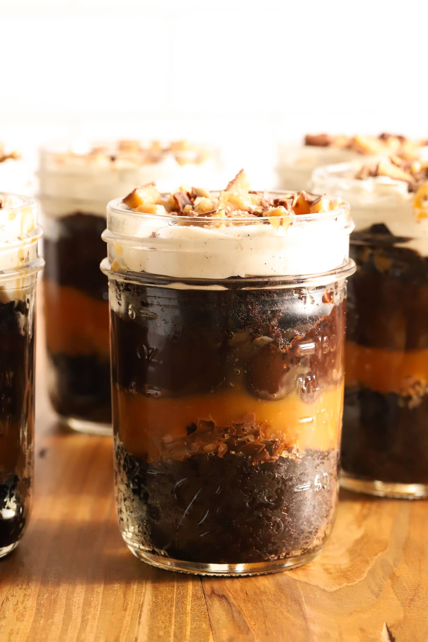 small jar of chocolate cake, chocolate pudding, whipped cream and caramel in layers. A spoon rests on top of the jar with a spoonful of crushed toffee candy bars on top.