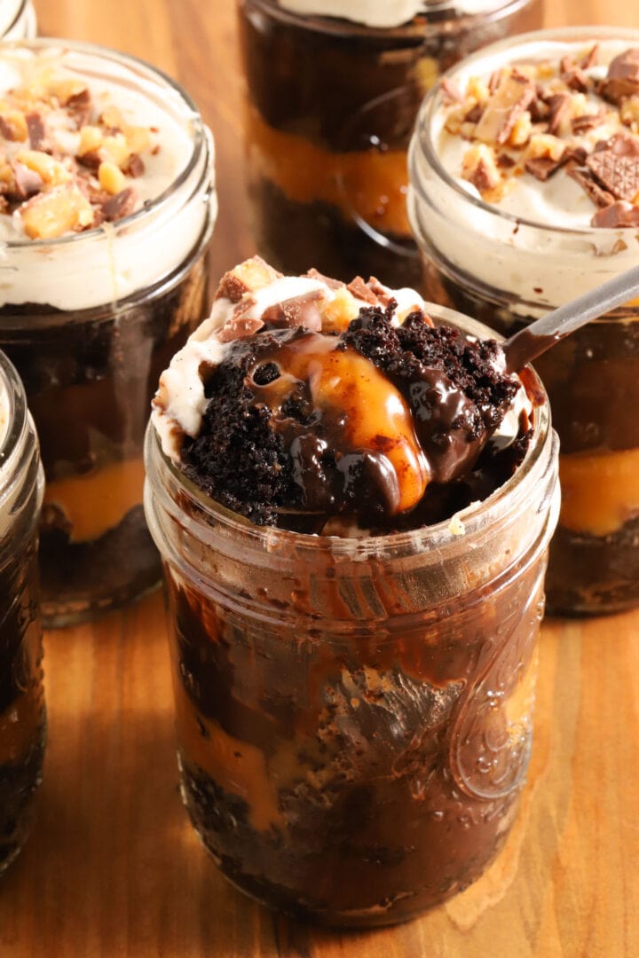 small jar of chocolate cake, chocolate pudding, whipped cream and caramel in layers. A spoon rests on top of the jar with a spoonful of everything on top of it.