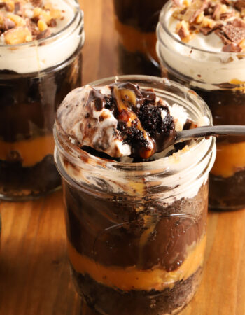 small jar of chocolate cake, chocolate pudding, whipped cream and caramel in layers. A spoon rests on top of the jar with a spoonful of everything on top of it.