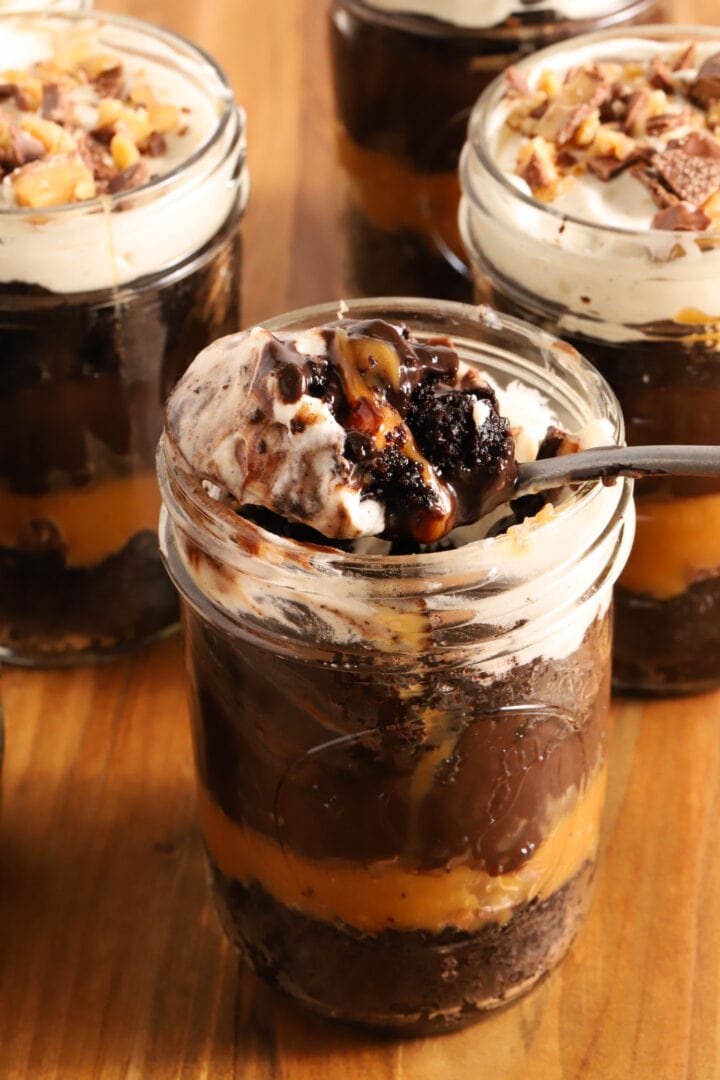 small jar of chocolate cake, chocolate pudding, whipped cream and caramel in layers. A spoon rests on top of the jar with a spoonful of everything on top of it.