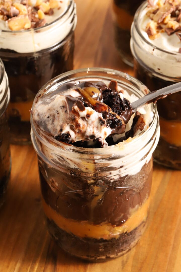 small jar of chocolate cake, chocolate pudding, whipped cream and caramel in layers. A spoon rests on top of the jar with a spoonful of everything on top of it.