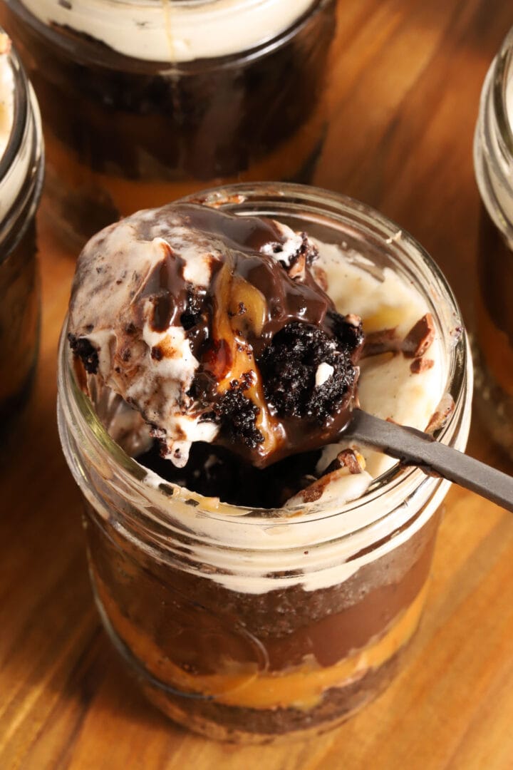 small jar of chocolate cake, chocolate pudding, whipped cream and caramel in layers. A spoon rests on top of the jar with a spoonful of everything on top of it.