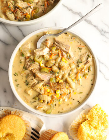 white bowl of creamy turkey soup with vegetables, gnocchi and corn muffins on the side