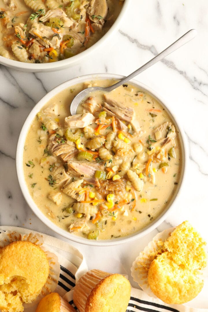 white bowl of creamy turkey soup with vegetables, gnocchi and corn muffins on the side