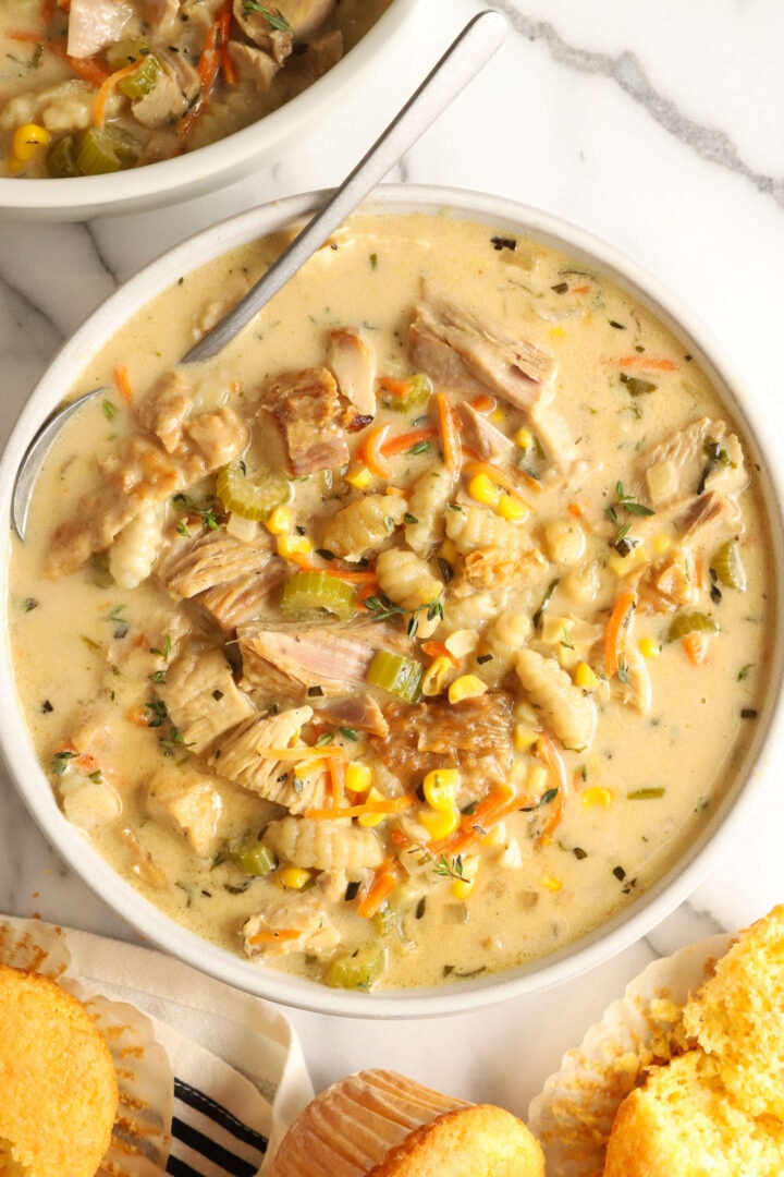 white bowl of creamy turkey soup with vegetables, gnocchi and corn muffins on the side