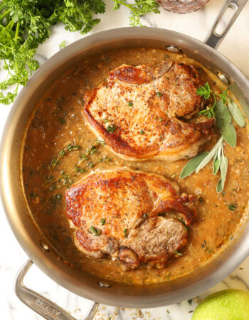 top view of two seared pork chops in a steel skillet, sprinkled with fresh thyme leaves