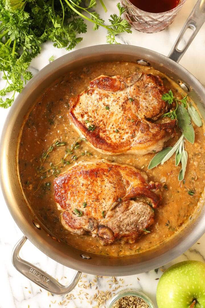 top view of two seared pork chops in a steel skillet, sprinkled with fresh thyme leaves