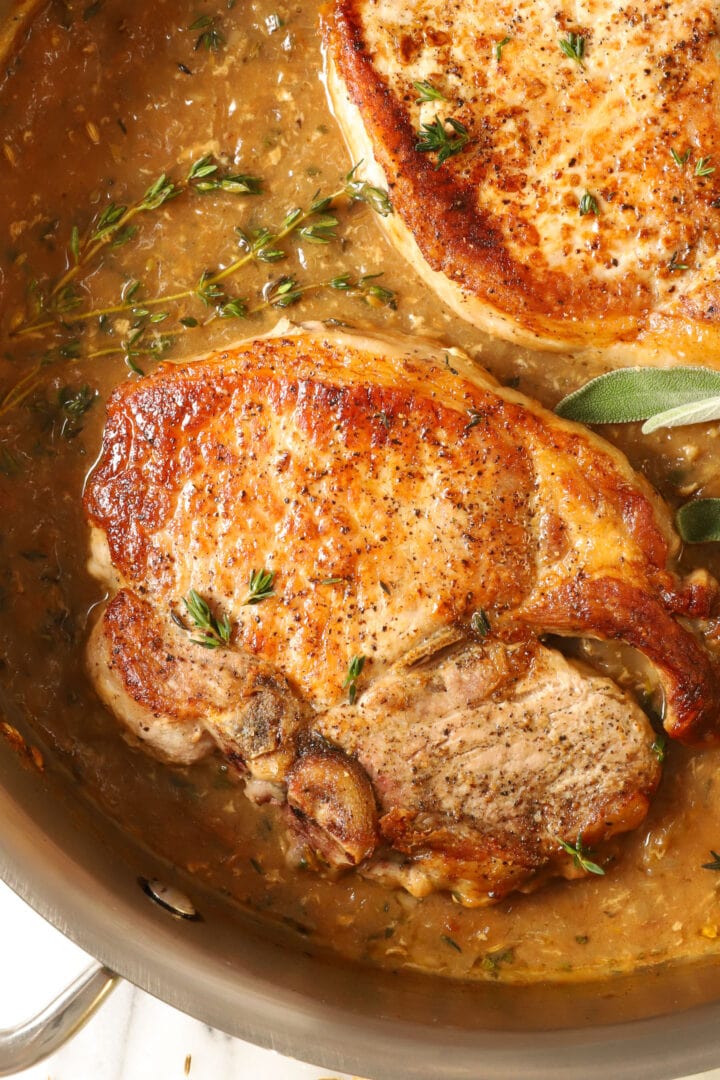 top view of a seared pork chop in a steel skillet, sprinkled with fresh thyme leaves