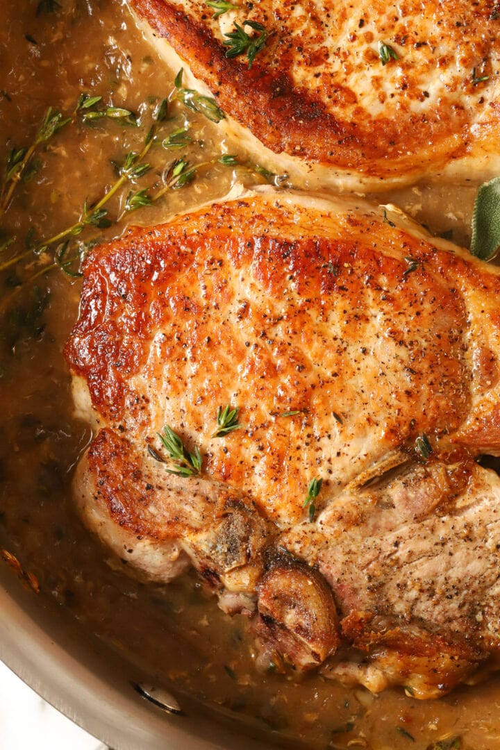 top view of a seared pork chop in a steel skillet, sprinkled with fresh thyme leaves