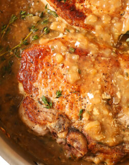 top view of a seared pork chop in a steel skillet, the pork chop is covered in a brown colored pan sauce and sprinkled with fresh thyme leaves