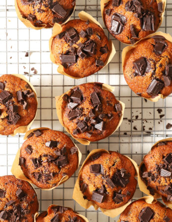 pumpkin chocolate chip muffins, sitting on a cooling rack in a brown paper wrapper.