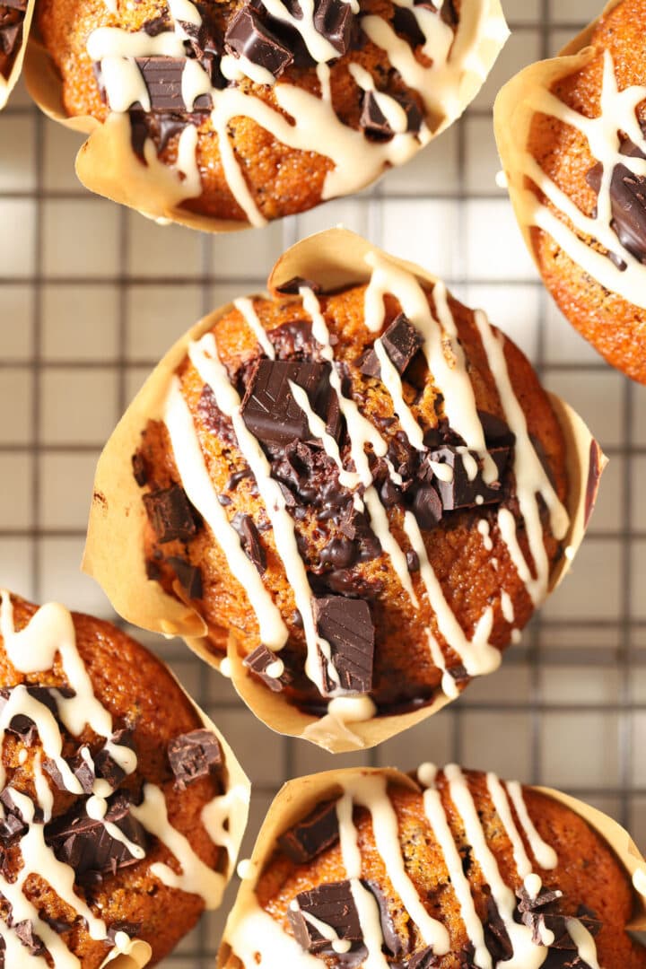 pumpkin chocolate chip muffin with a white glaze drizzled on top, sitting on a cooling rack in a brown paper wrapper.