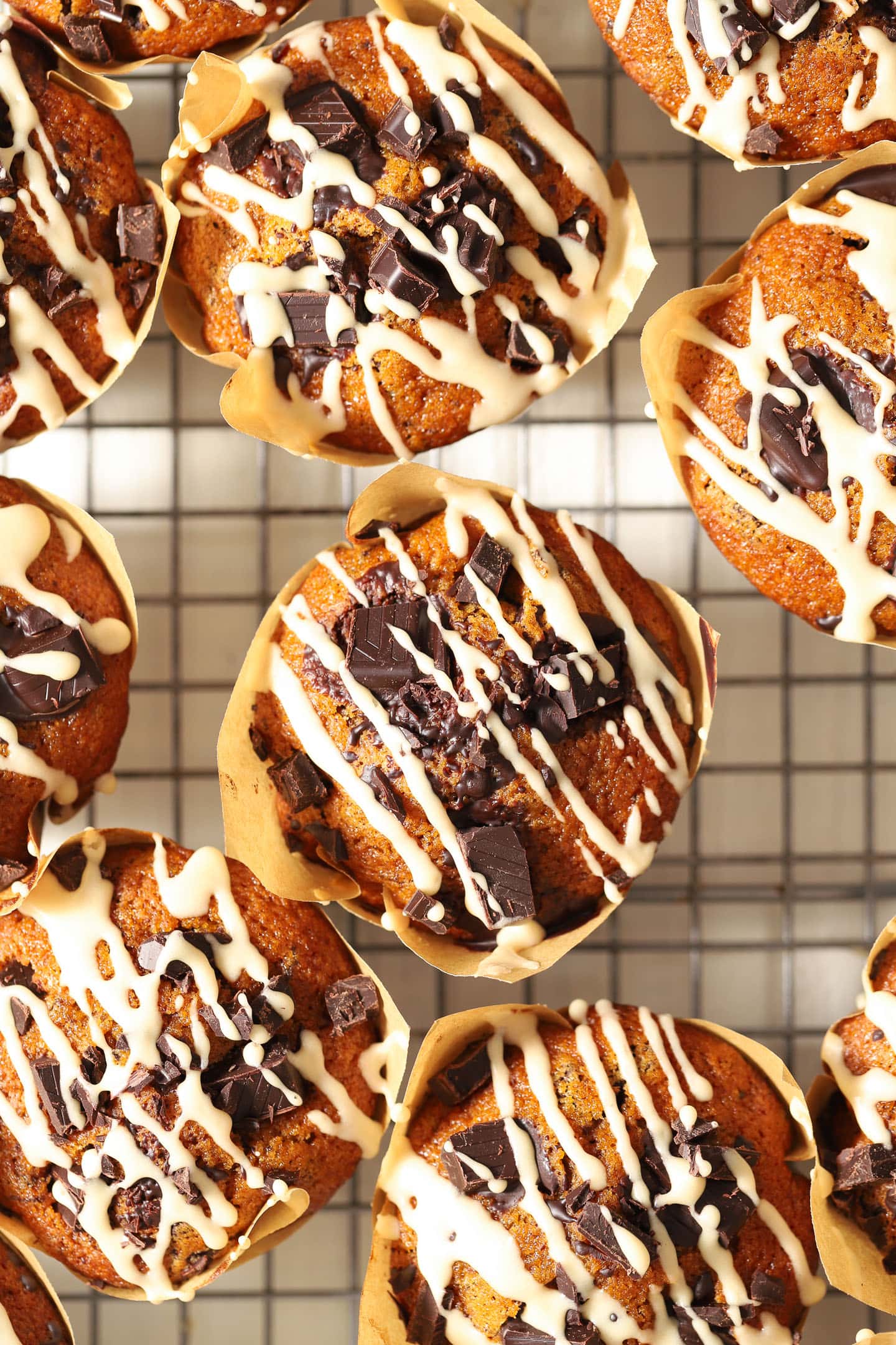 pumpkin chocolate chip muffins with a white glaze drizzled on top, sitting on a cooling rack in a brown paper wrapper.