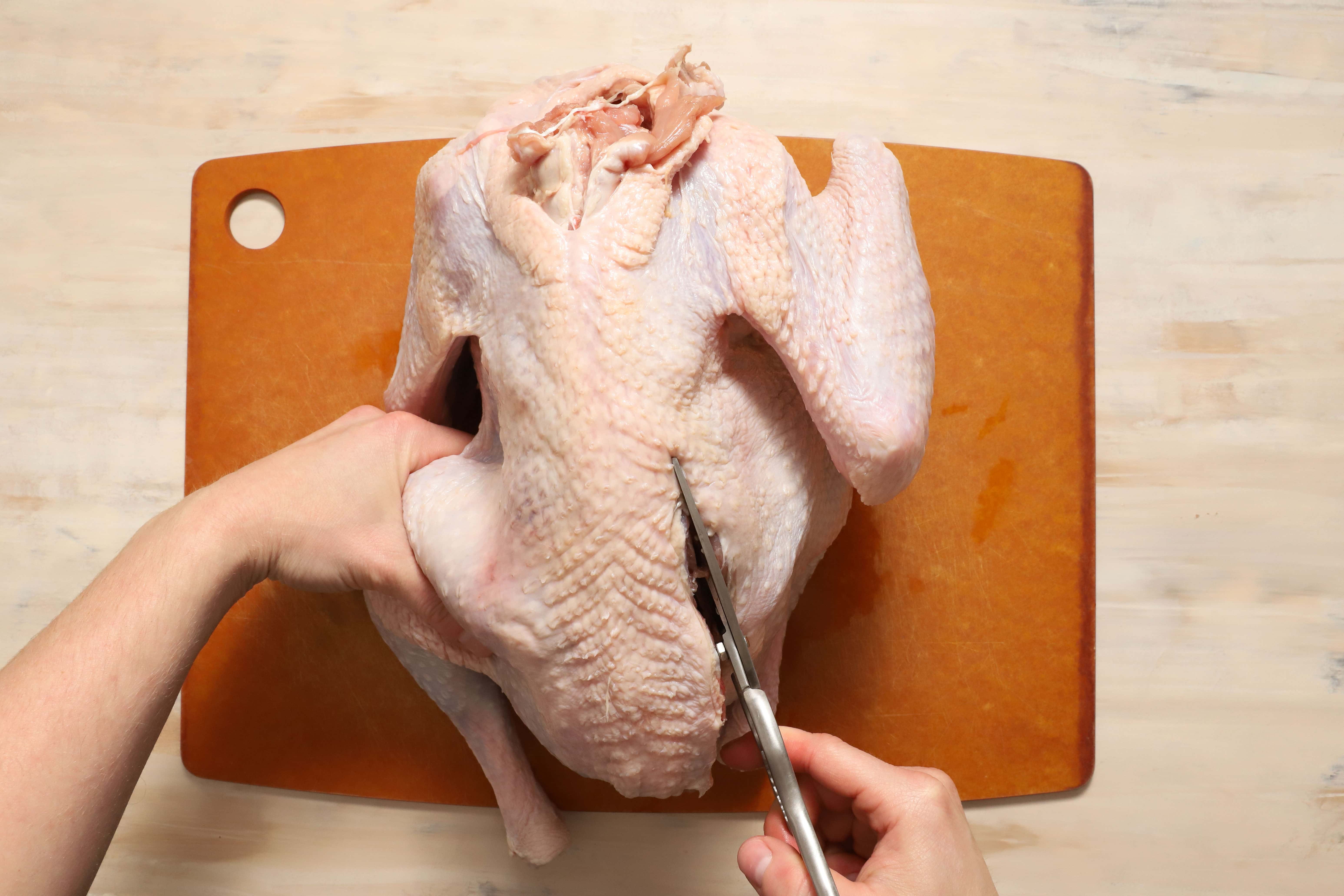 a pair of hands demonstrating how to remove the backbone of a turkey before roasting