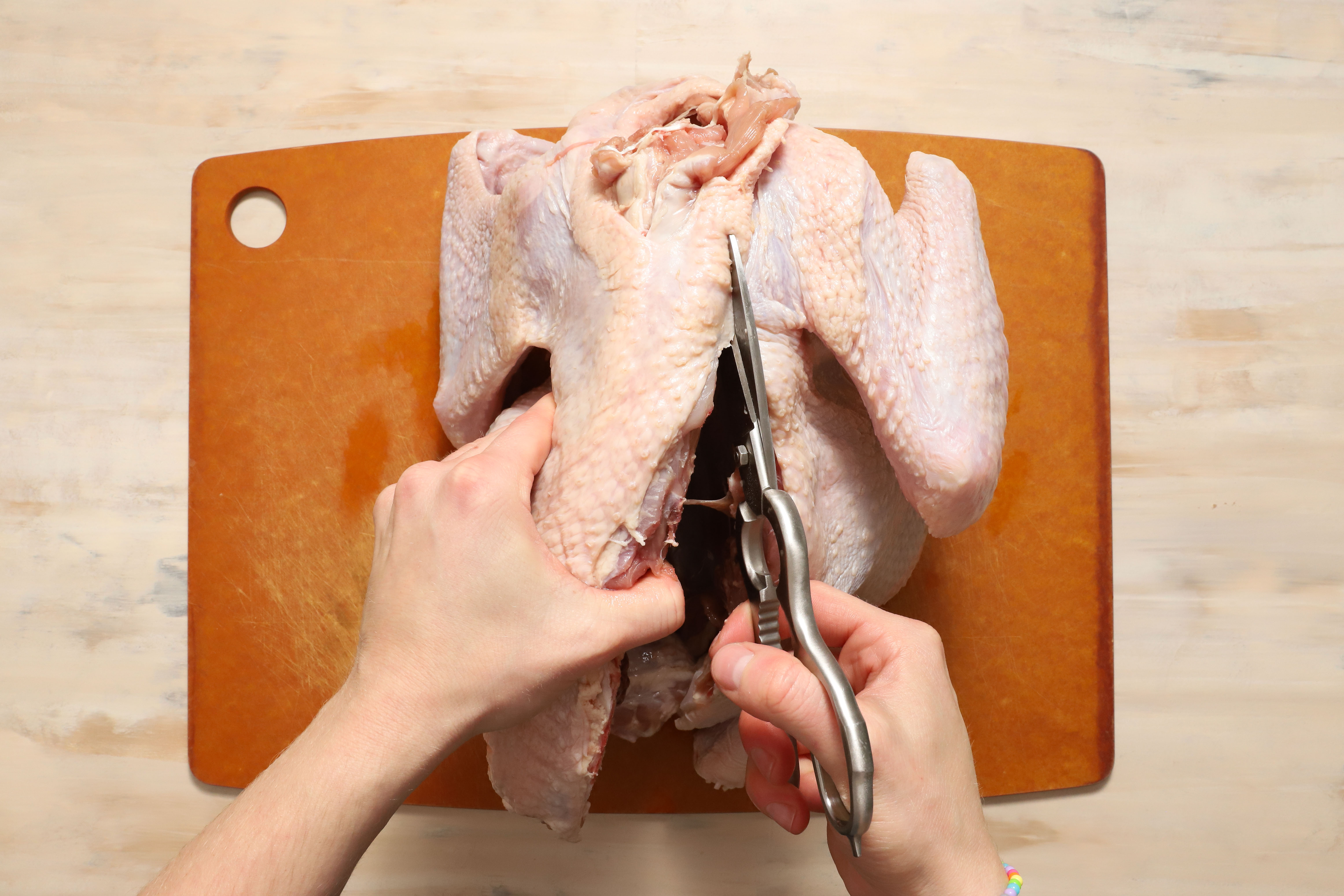 a pair of hands demonstrating how to remove the backbone of a turkey before roasting