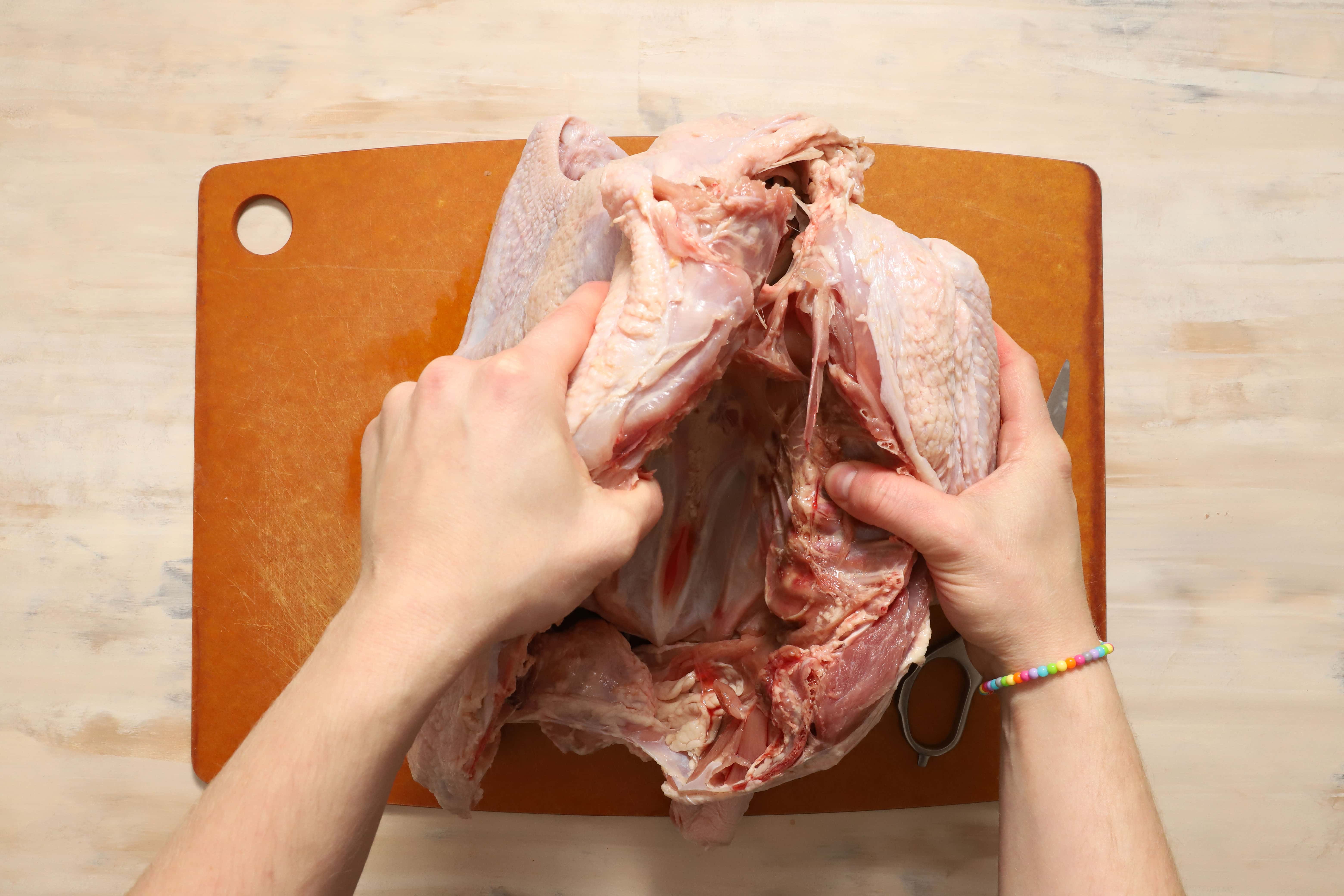 a pair of hands demonstrating how to remove the backbone of a turkey before roasting