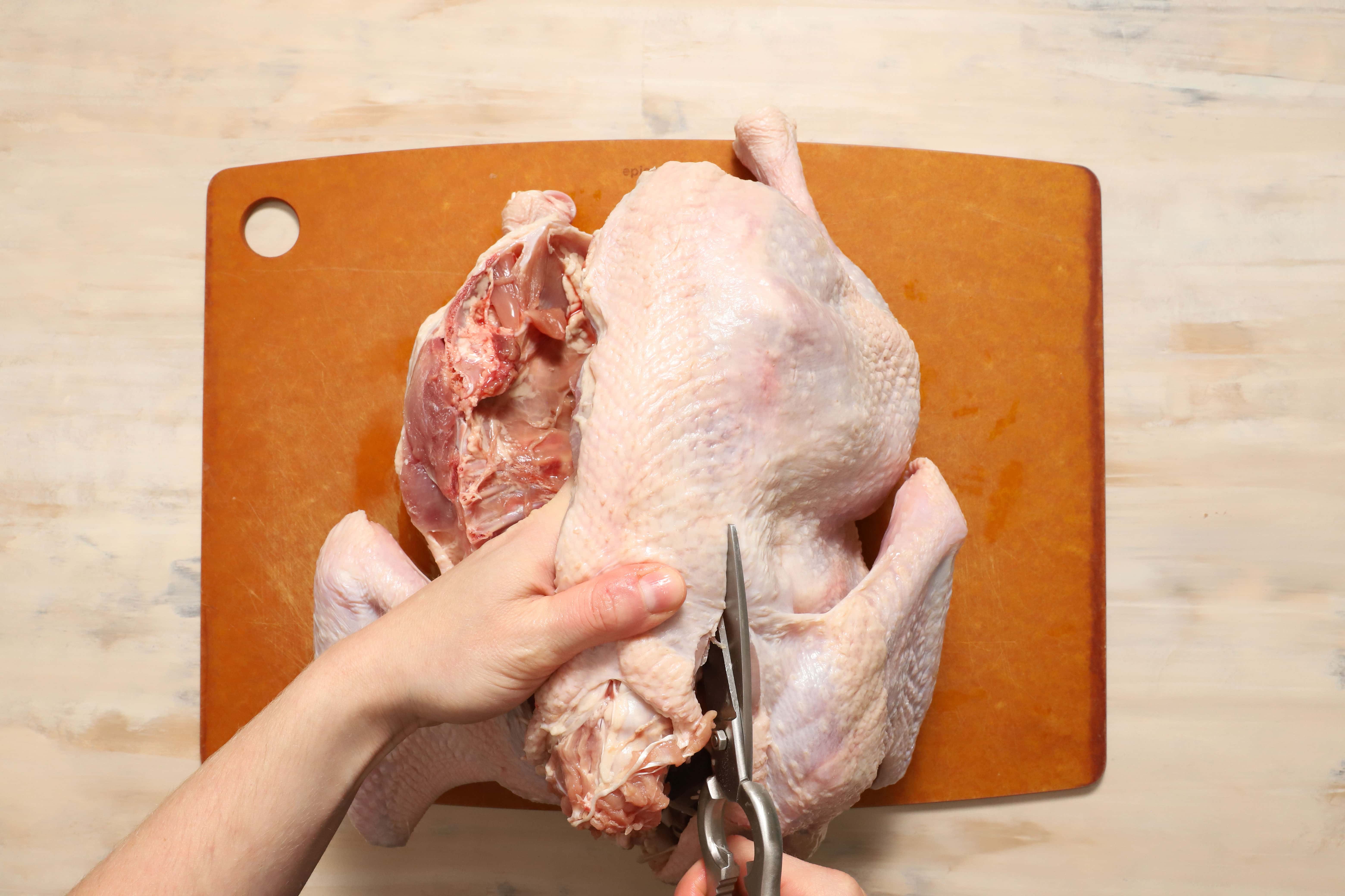 a pair of hands demonstrating how to remove the backbone of a turkey before roasting