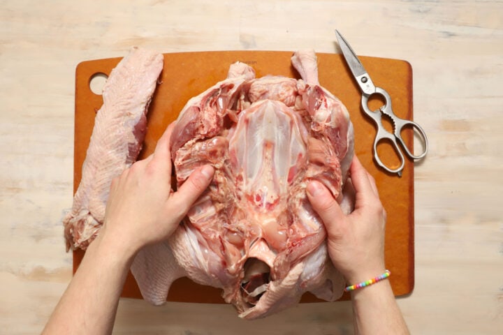 a pair of hands demonstrating how to remove the backbone of a turkey before roasting