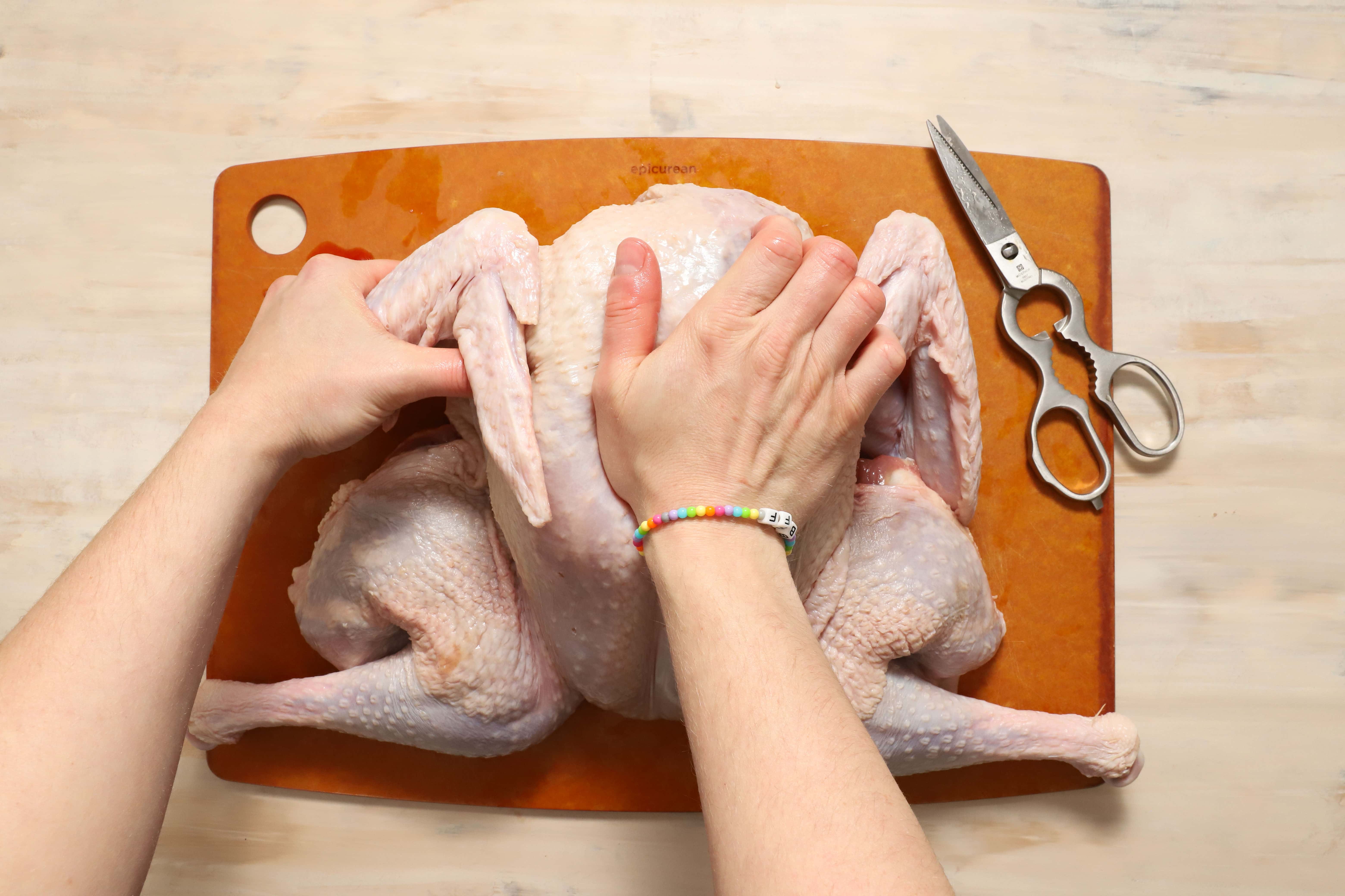 a pair of hands cracking down on the breastbone of the turkey