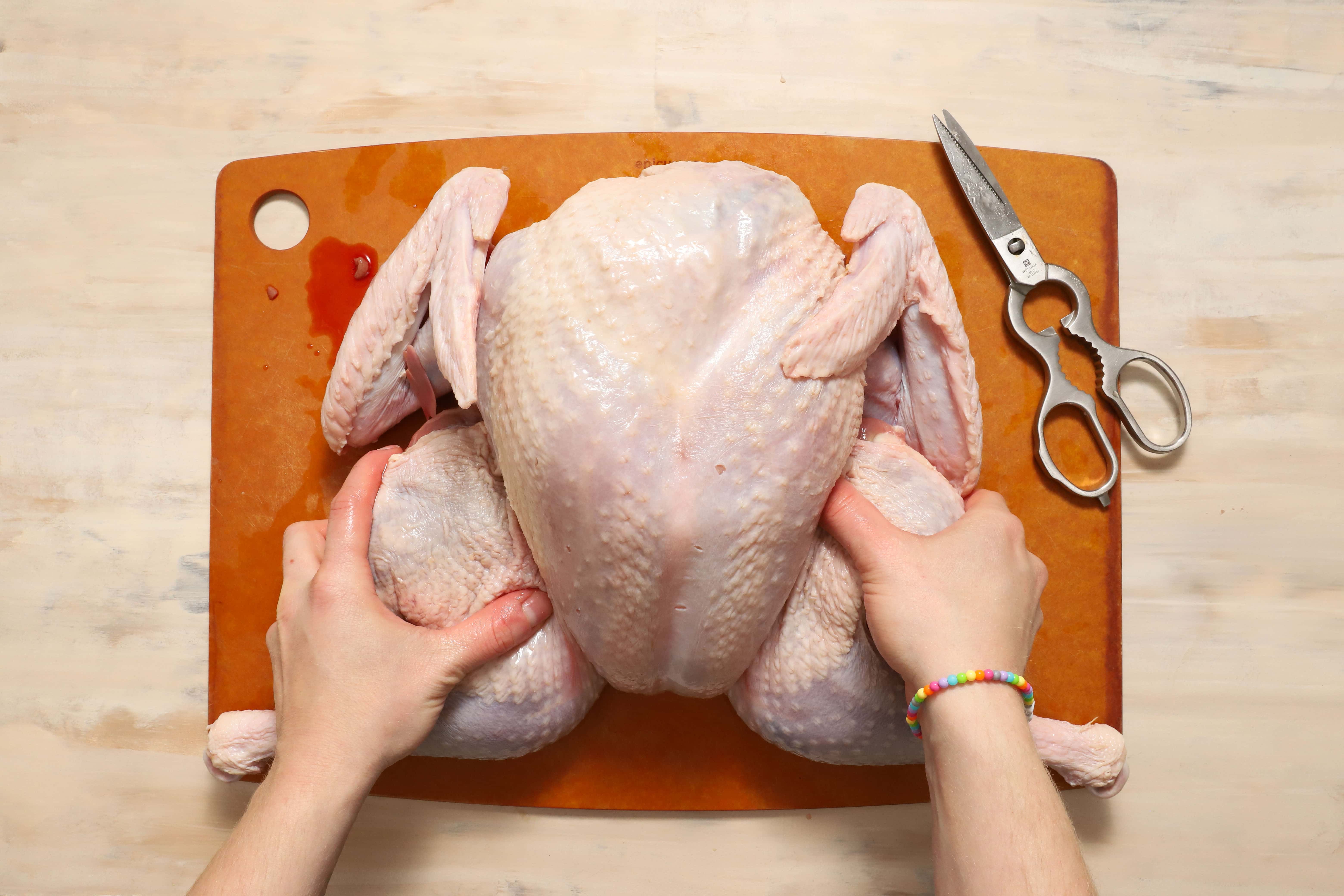 a pair of hands demonstrating how to position the thighs of the turkey before roasting