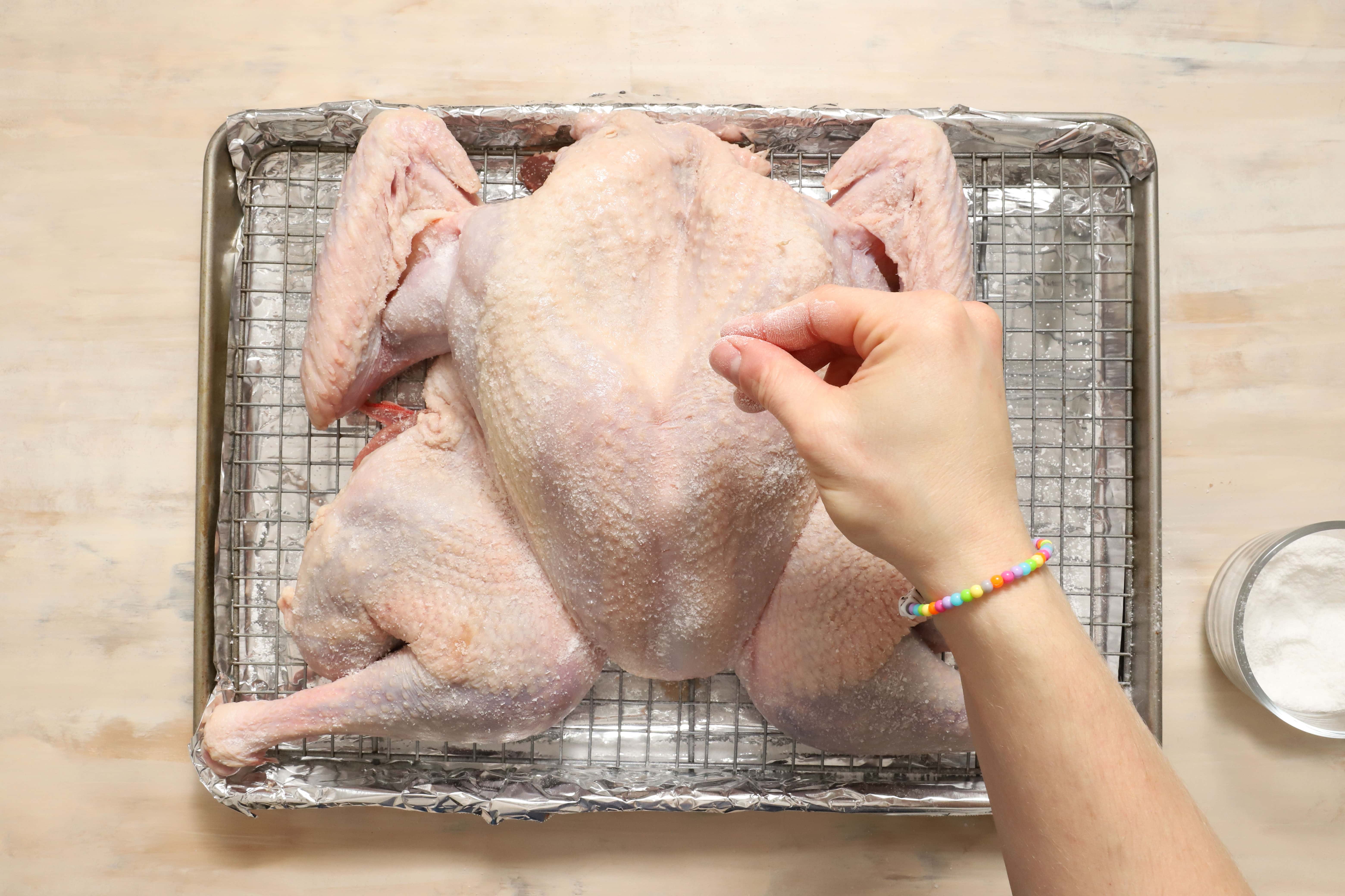 a salted turkey before being roasted, sitting on a silver metal rack