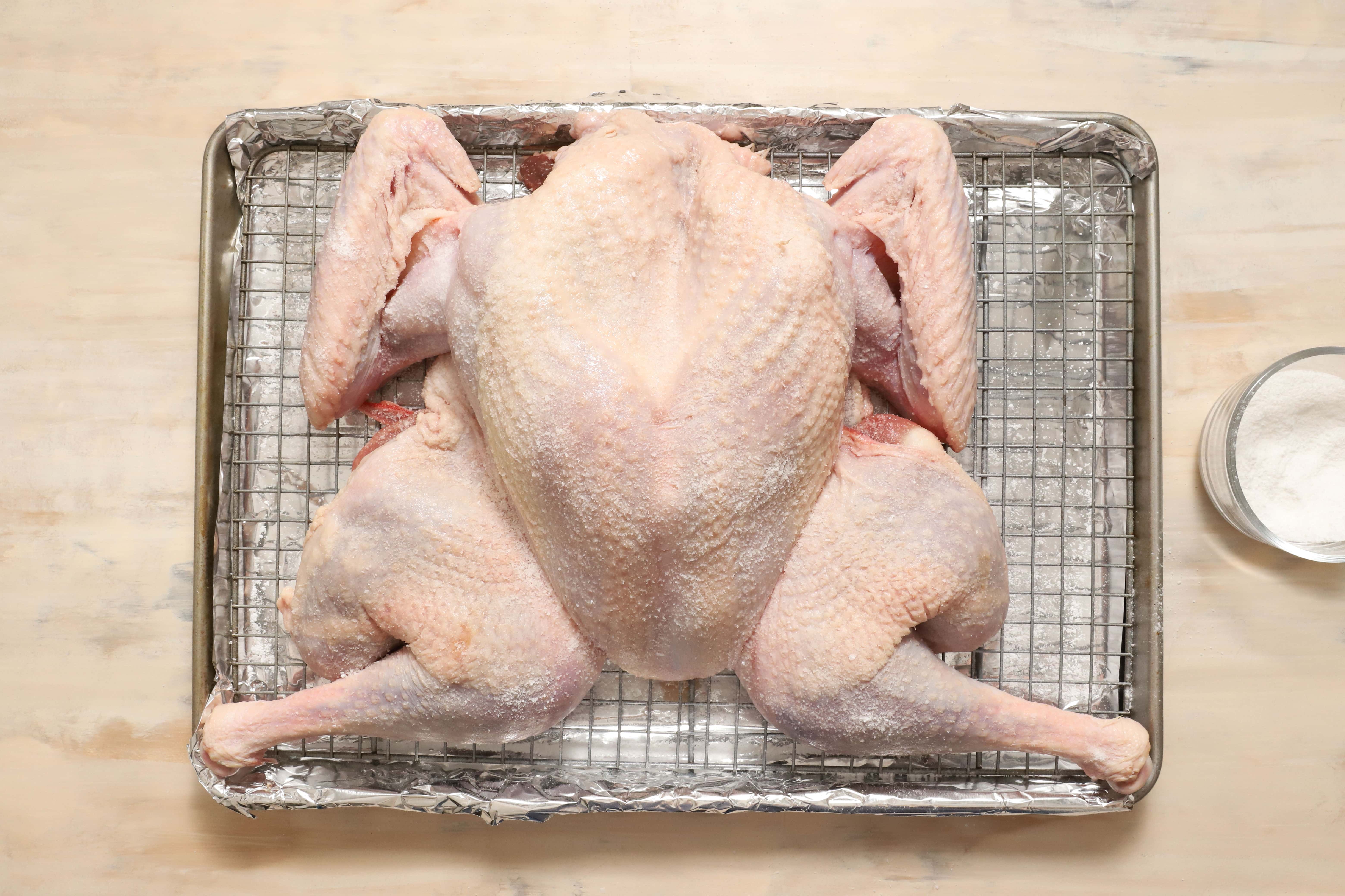 a salted turkey before being roasted, sitting on a silver metal rack