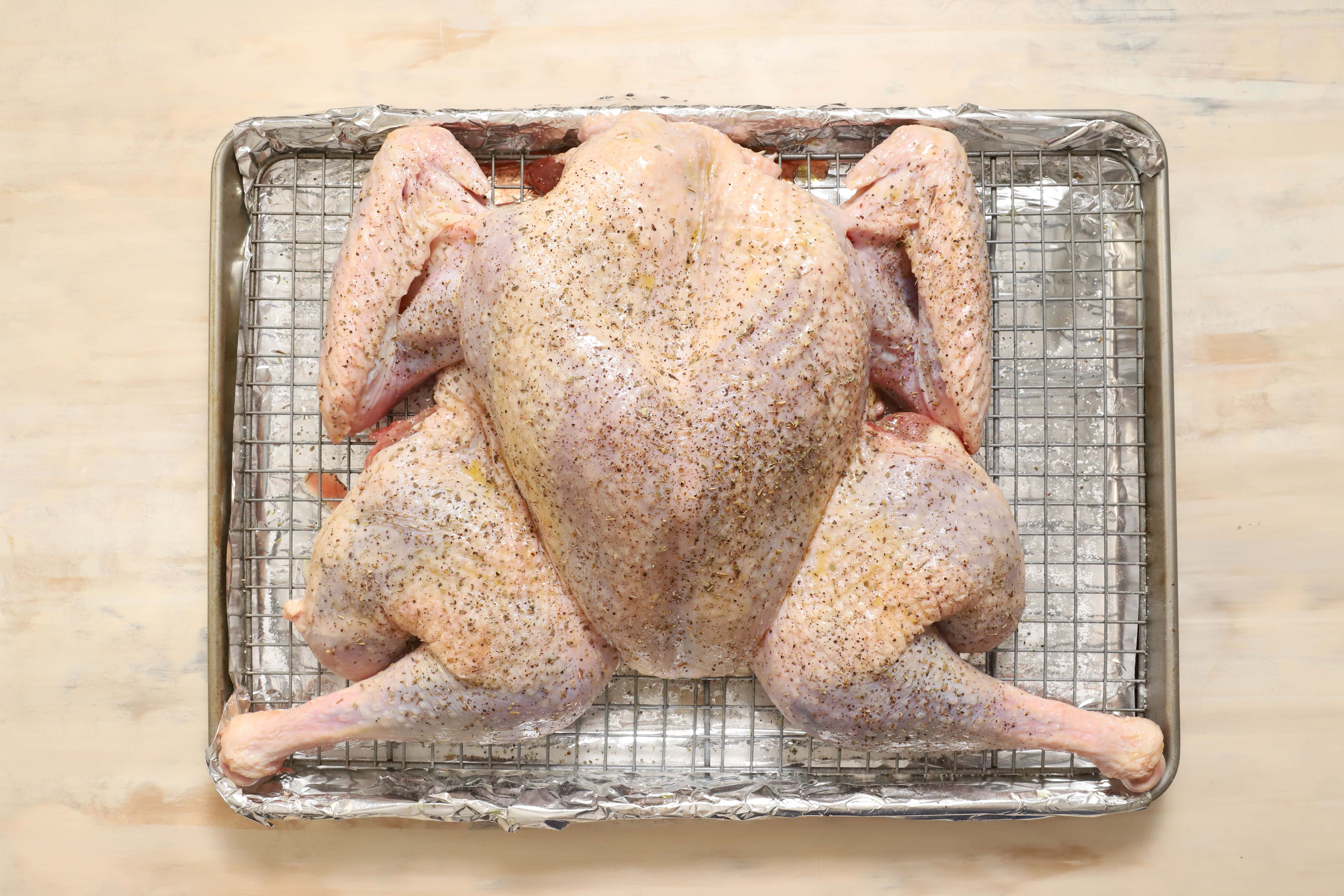 a whole, raw turkey that has been oiled and seasoned, sitting on a silver metal rack.