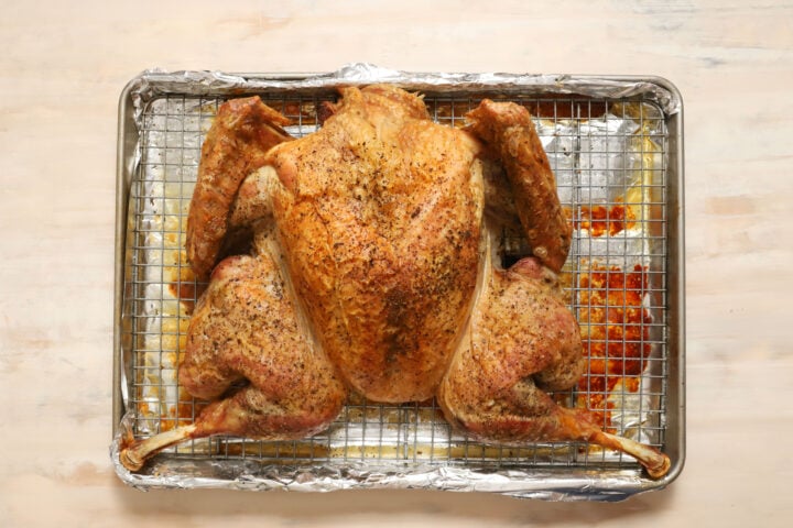 a whole roasted turkey sitting on a silver metal pan and cooling rack