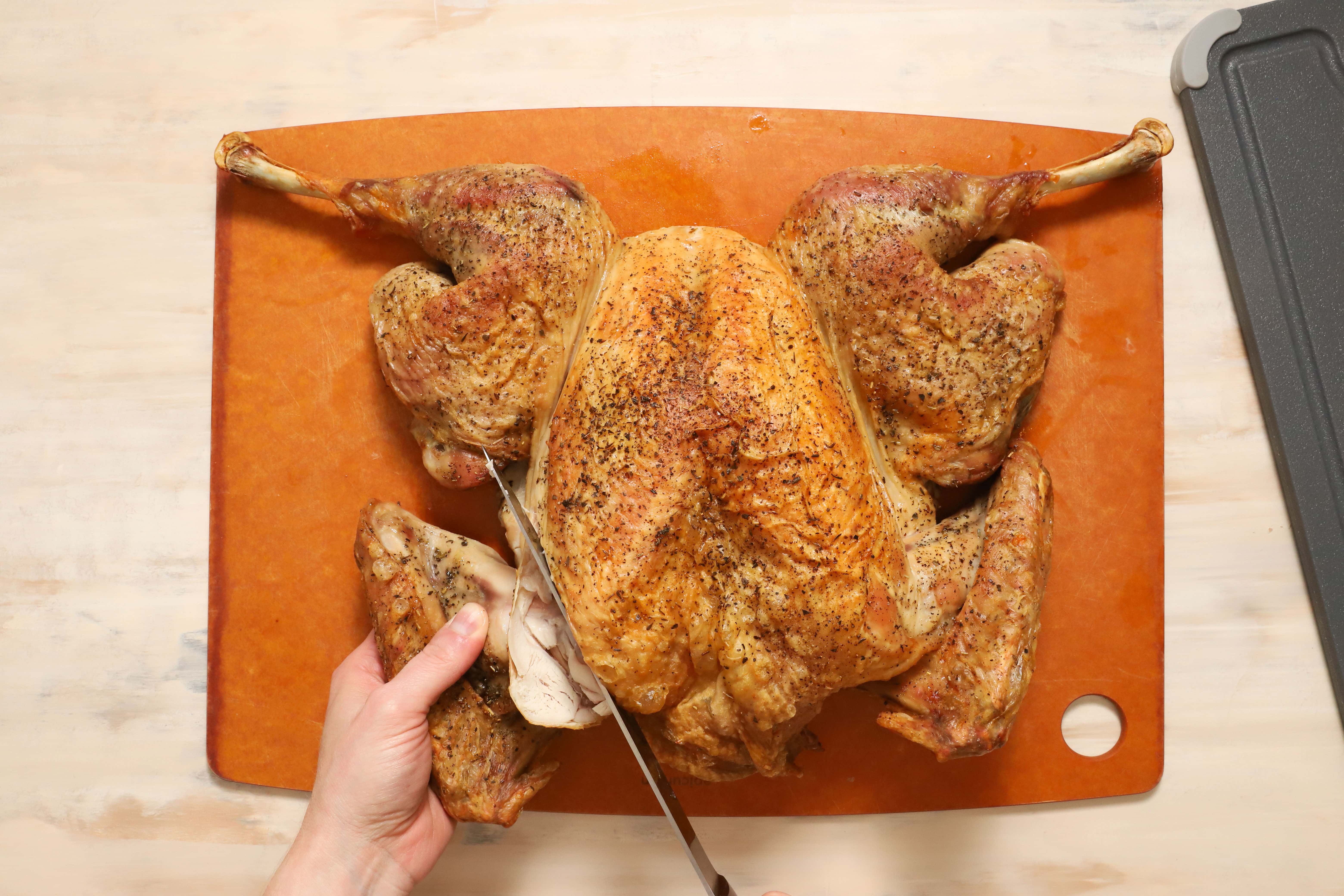 a pair of hands showing how to carve turkey wings away from the rest of the turkey