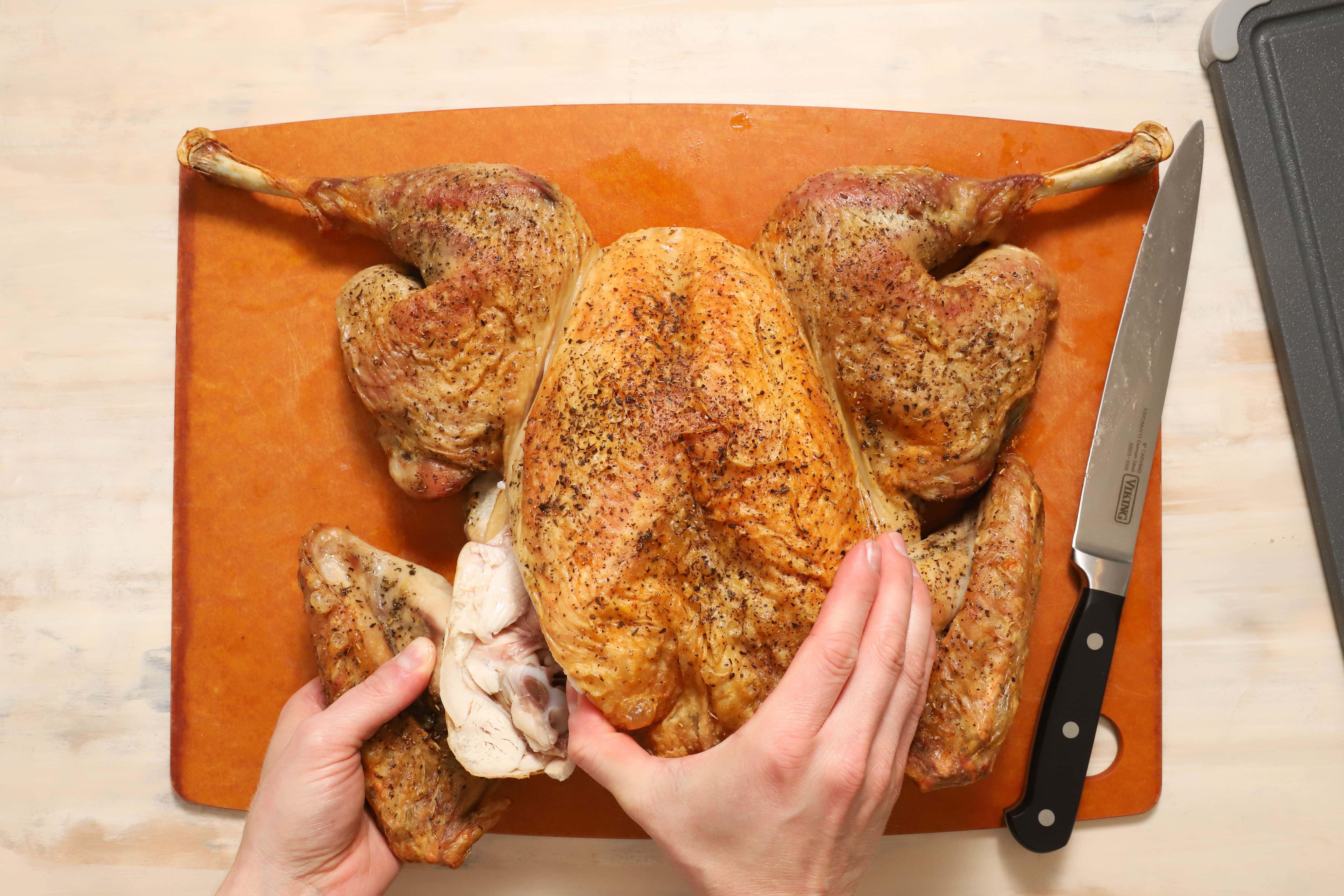 a pair of hands showing how to carve turkey wings away from the rest of the turkey