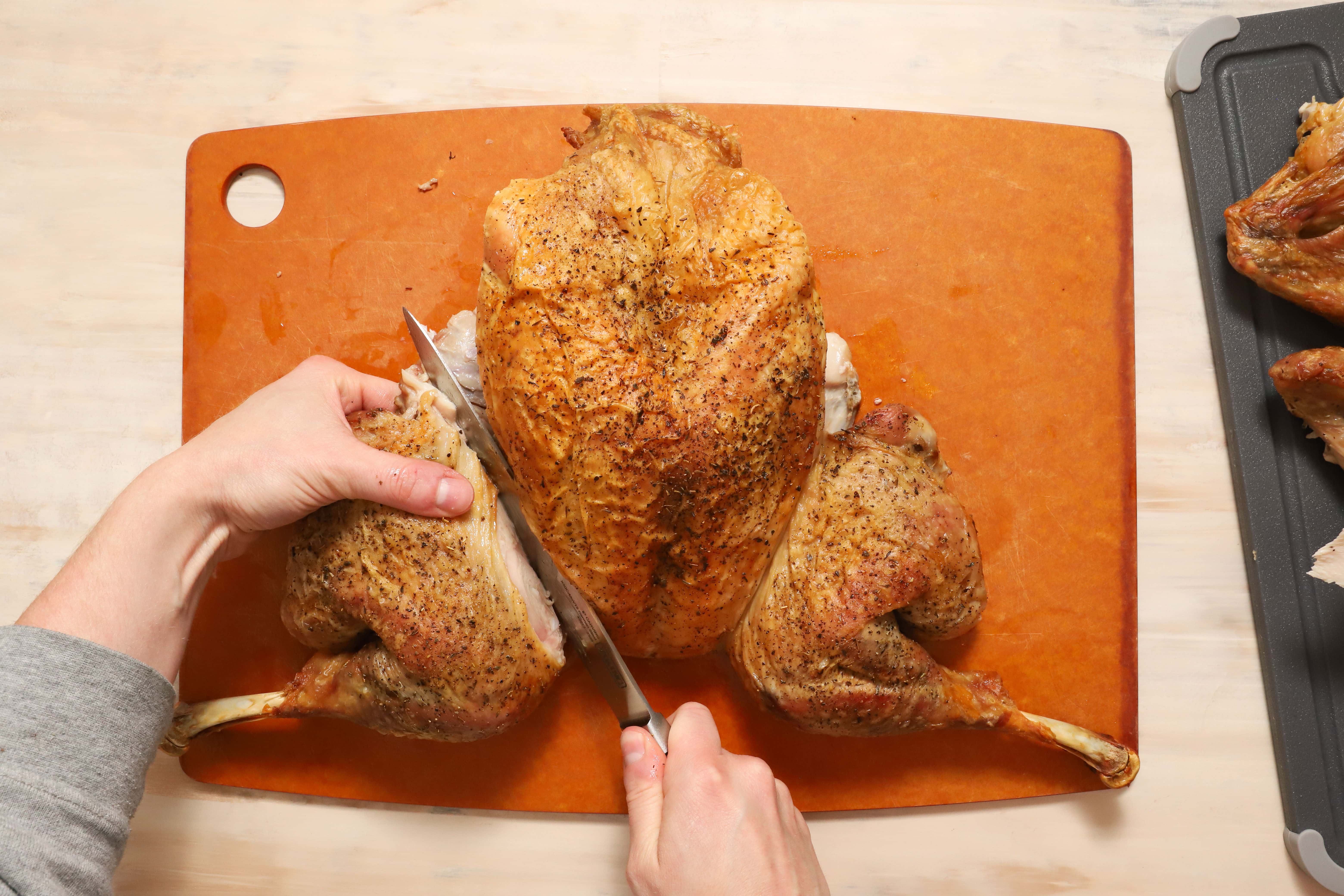 a pair of hands showing how to carve turkey thighs and drumsticks away from the rest of the turkey