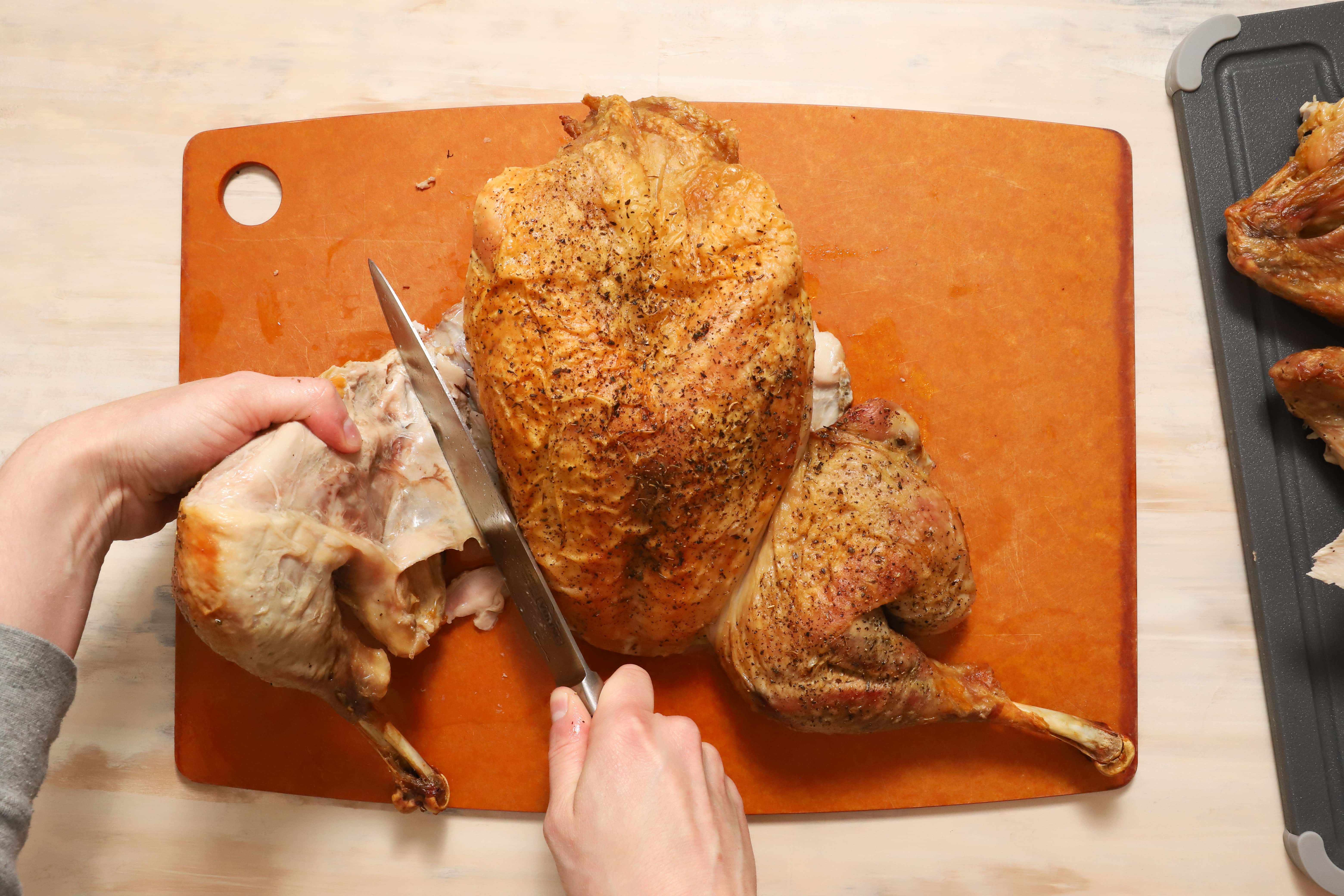 a pair of hands showing how to carve turkey thighs and drumsticks away from the rest of the turkey