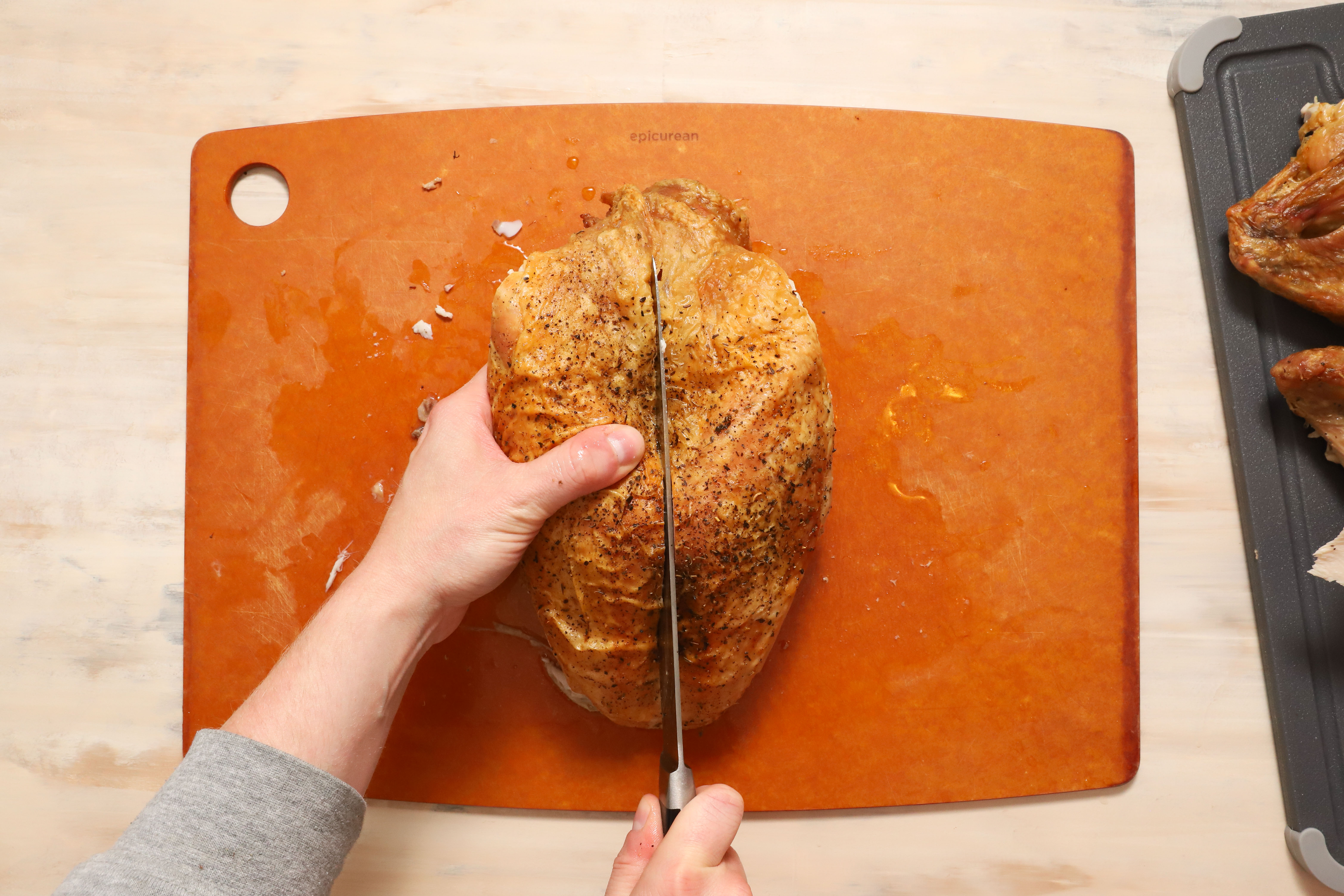 a pair of hands showing how to carve turkey breast meat away from the ribcage of the turkey