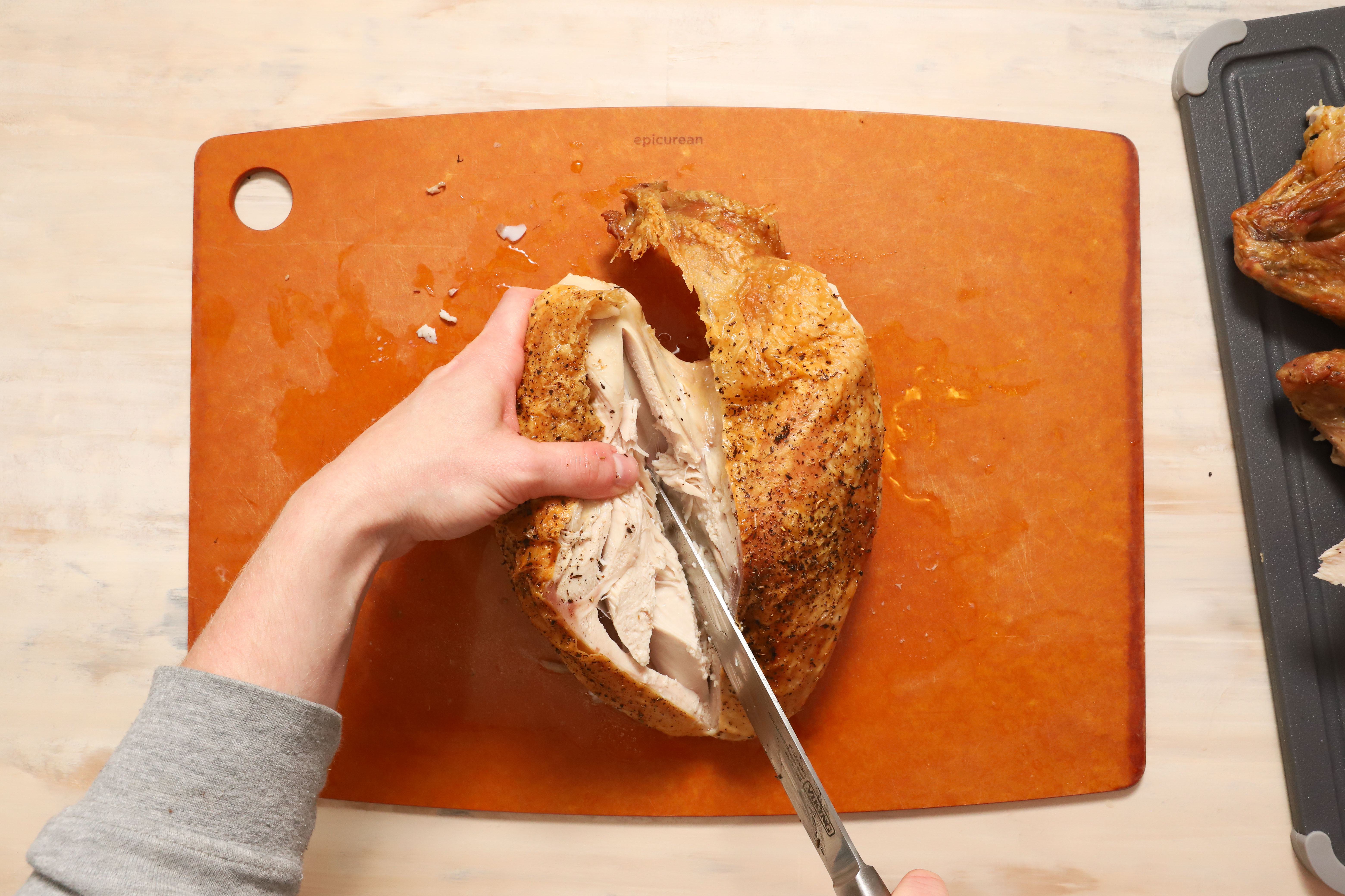 a pair of hands showing how to carve turkey breast meat away from the ribcage of the turkey