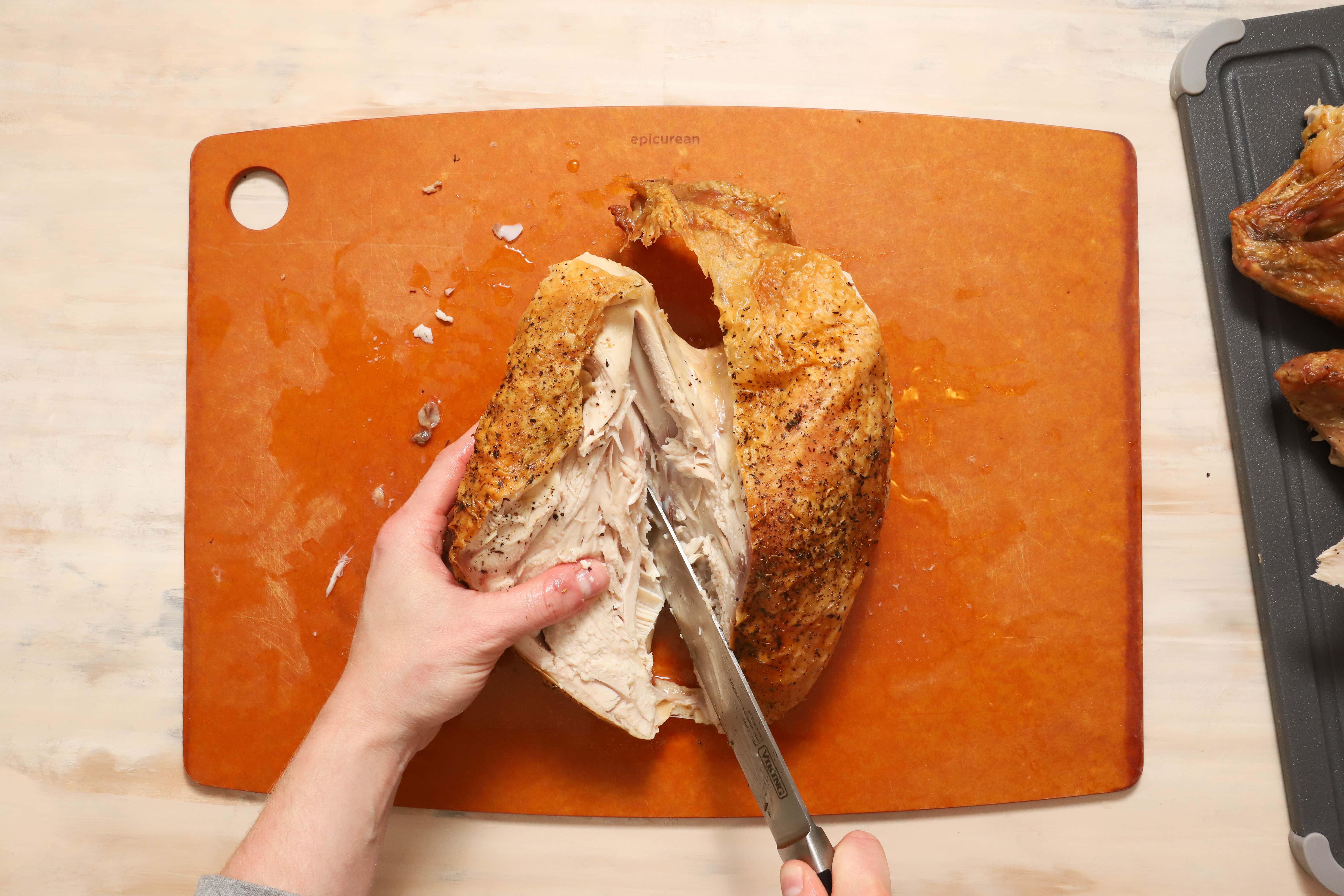 a pair of hands showing how to carve turkey breast meat away from the ribcage of the turkey