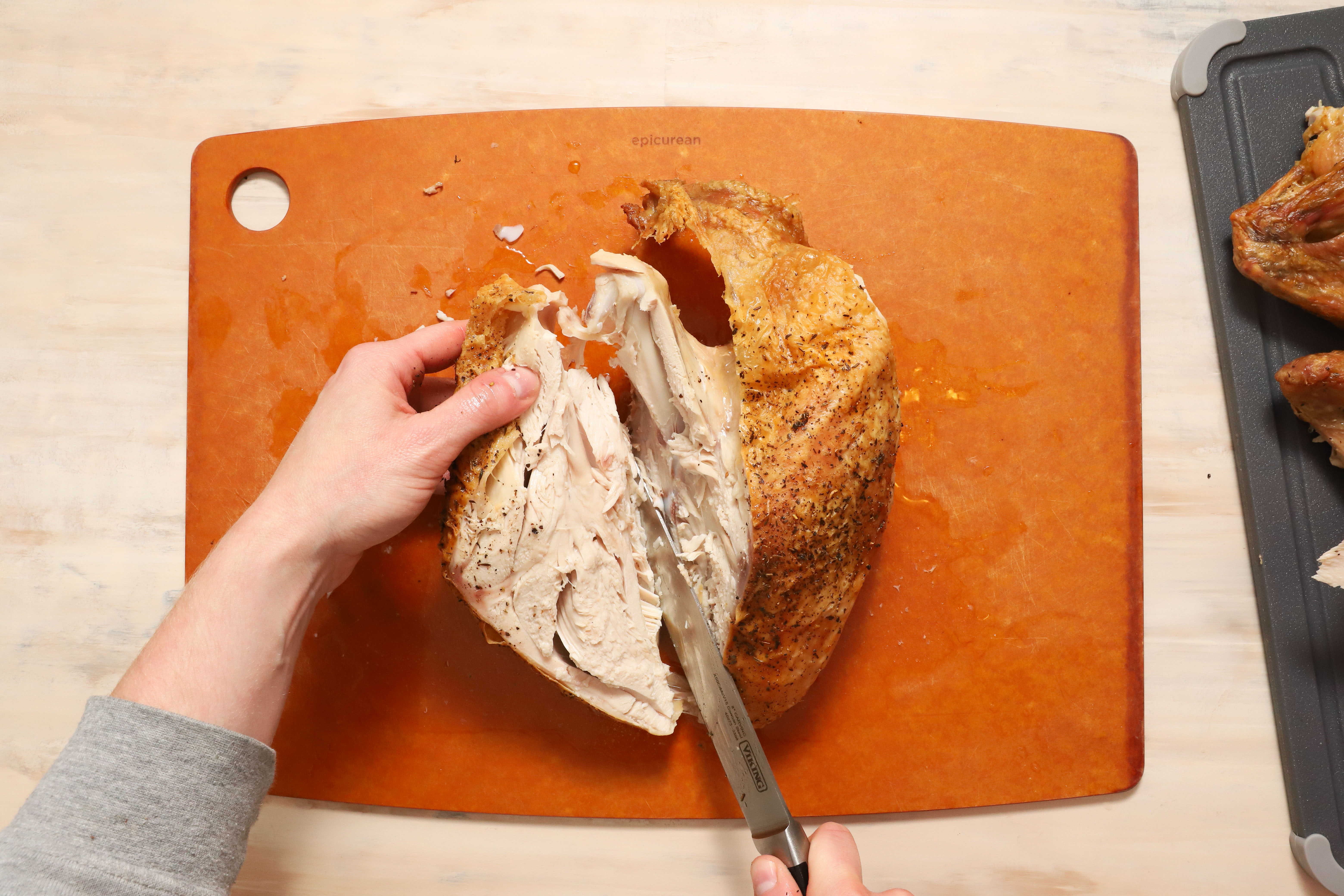 a pair of hands showing how to carve turkey breast meat away from the ribcage of the turkey