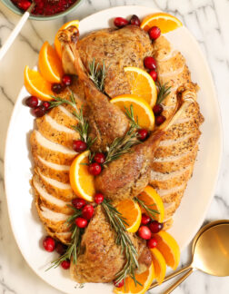 roasted and carved turkey on a white platter, garnished with fresh rosemary sprigs, cranberries and orange slices