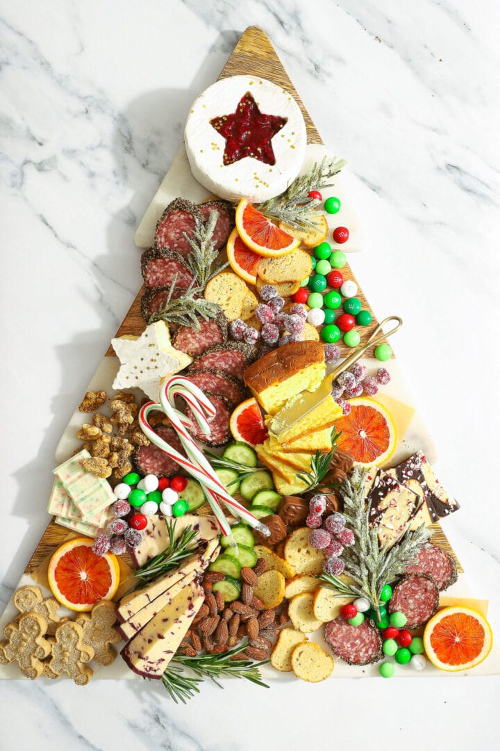 christmas tree shaped snack board topped with sweet, salty and savory snacks.