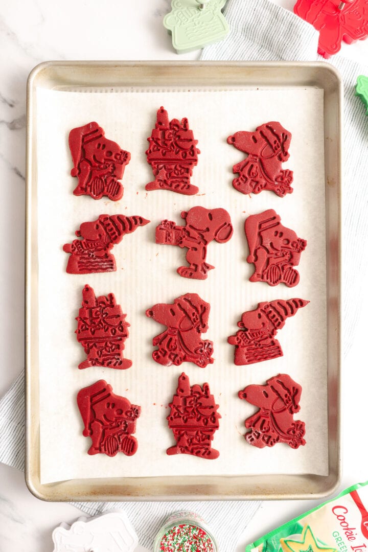 several unbaked red velvet cut out cookies shaped like snoopy and christmas trees.