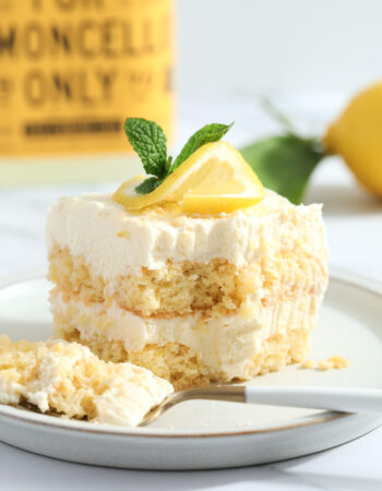 slice of lemon tiramisu that is garnished with a twisted slice of lemon and a sprig of fresh mint.