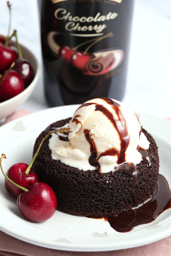 a small chocolate cake on a white plate topped with vanilla ice cream and garnished with fresh cherries.