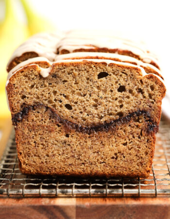 front view of a loaf of cinnamon banana bread with a bunch of bananas in the background