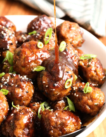 white bowl of teriyaki meatballs with green onions and sesame seeds.