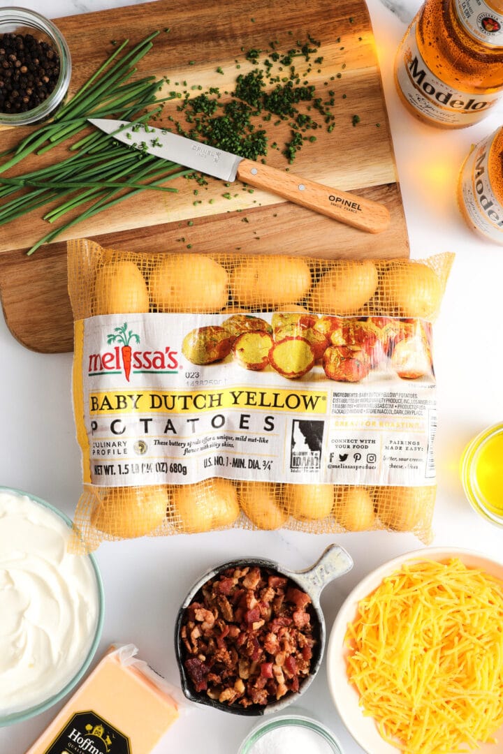 all of the ingredients to make loaded smashed potatoes, including baby yellow potatoes, chives, sour cream, bacon and cheese.