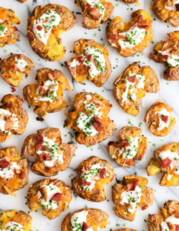 top view of a batch of loaded smashed potatoes that are covered in sour cream, cheese and bacon bits.