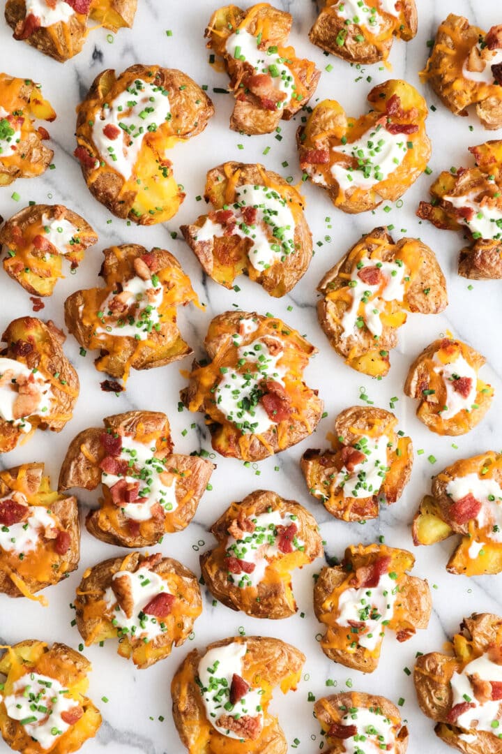 top view of a batch of loaded smashed potatoes that are covered in sour cream, cheese and bacon bits.